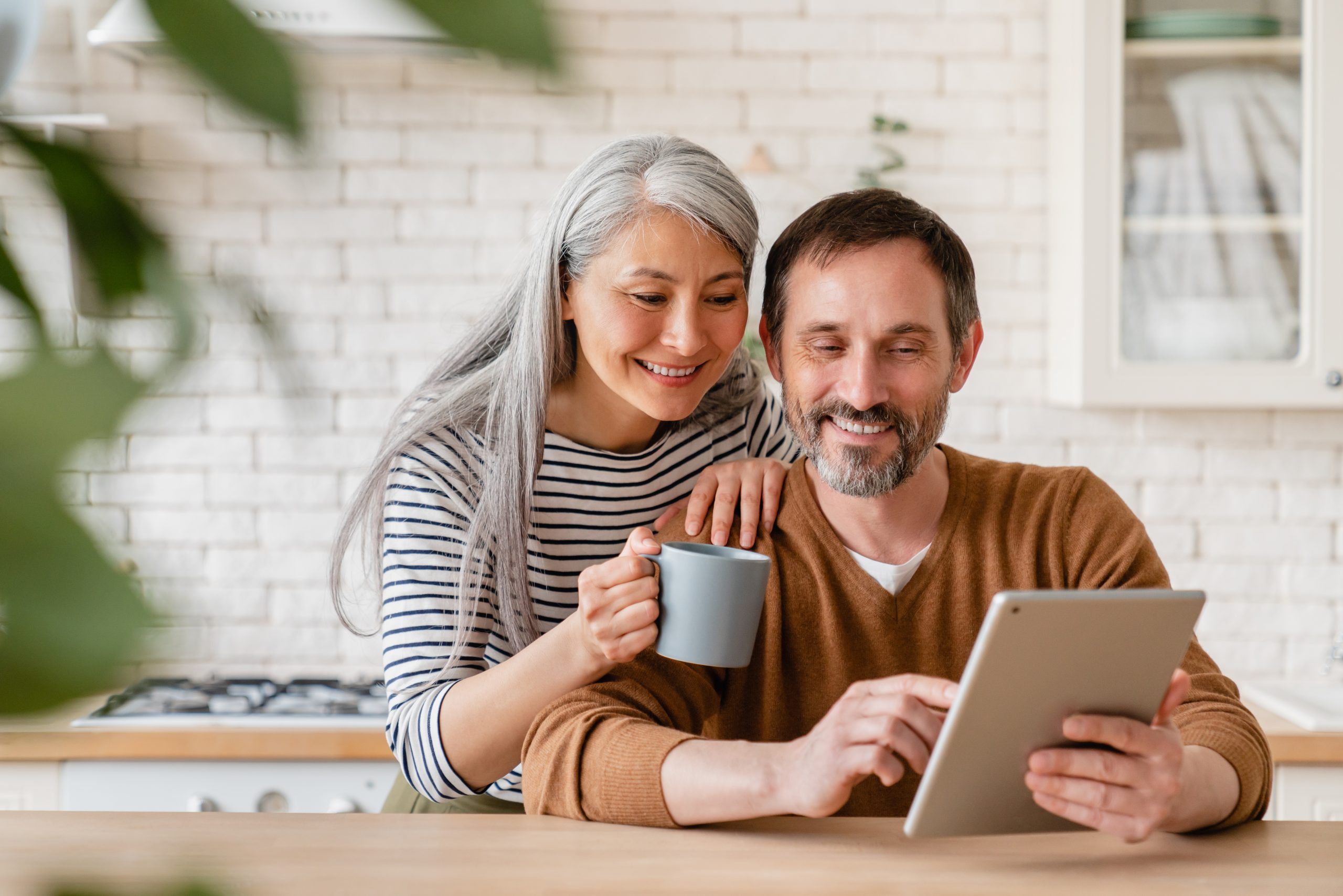 Happy mature middle-aged family couple parents husband and wife checking emails, reading news on digital tablet during breakfast, choosing new house, using application online