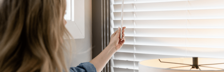 woman opening blinds in bedroom next to a lamp