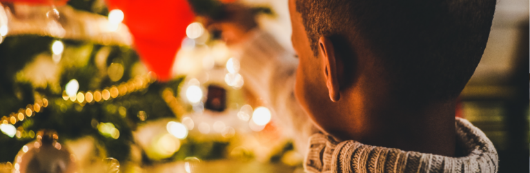 Back of child's head while attaching an ornament to a Christmas tree