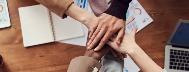 Coworkers stack their hands over a conference table.
