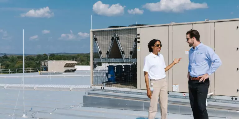 Two business professionals talk beside rooftop HVAC equipment.