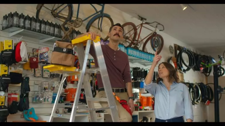Two people inspect overhead equipment in a bicycle shop.