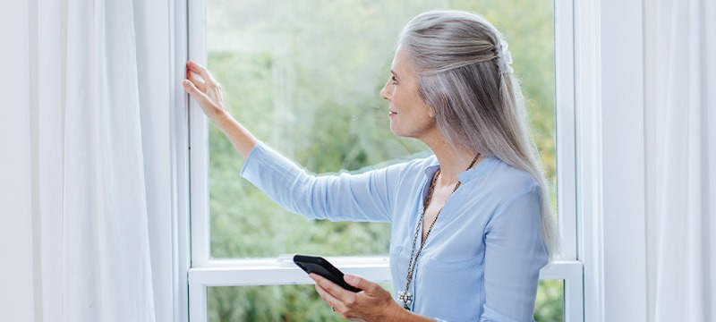 Woman standing in front of a window, checking for air leaks.