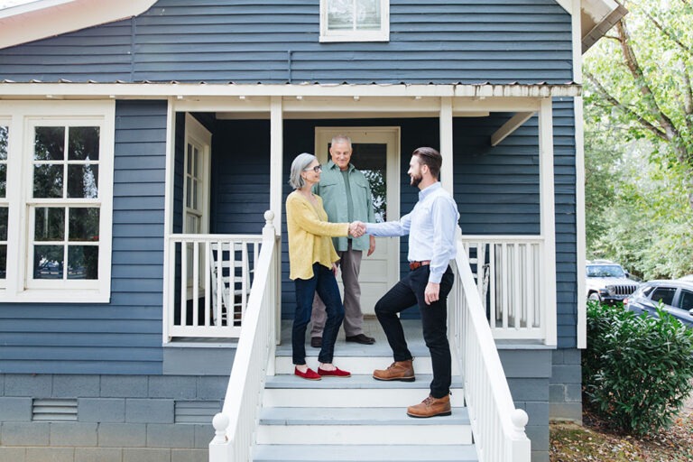 Couple in front of blue house, shaking hands with a TVA EnergyRight home energy expert.