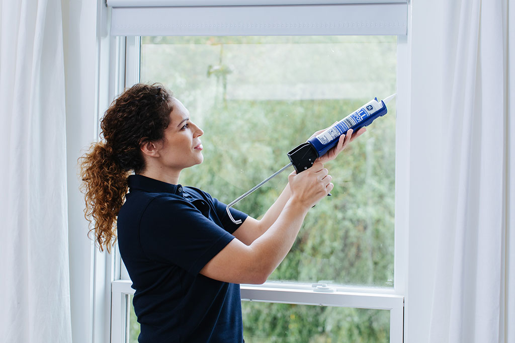 Woman caulking window.