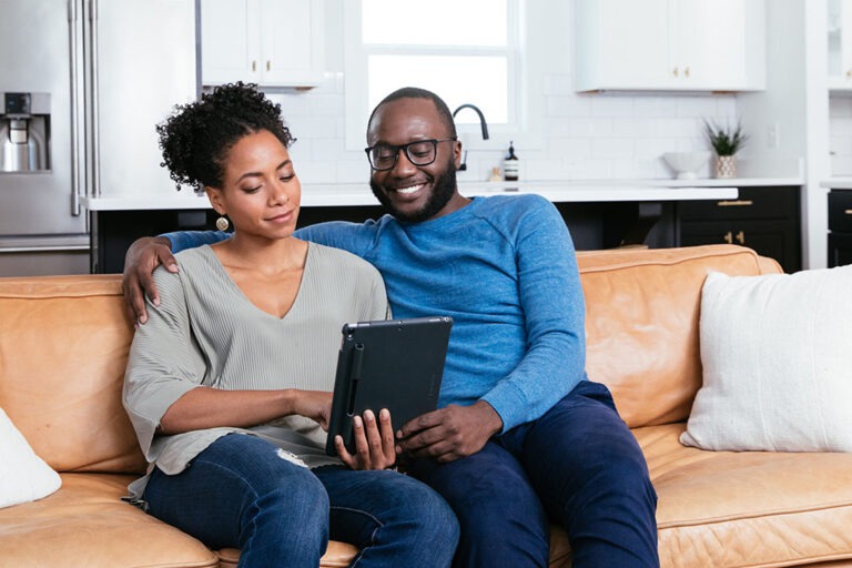 Couple on couch, looking at a tablet, thinking about home energy improvements.