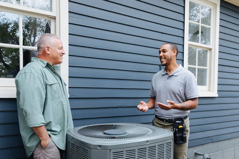 two men disucucssing HVAC improvements outside a blue home.