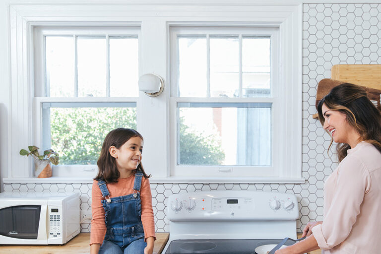 mother and daughter in kitchen, in front of a bright window.