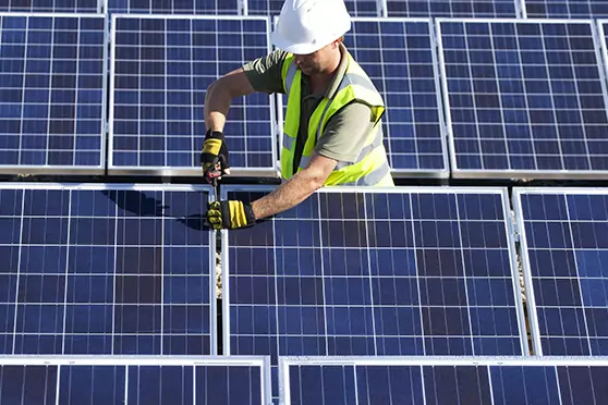 Man wearing a safety vest and white hard hat installing a solar array.