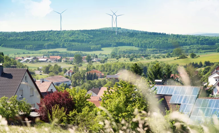 Image of a valley with home solar panels and wind turbines in the background.