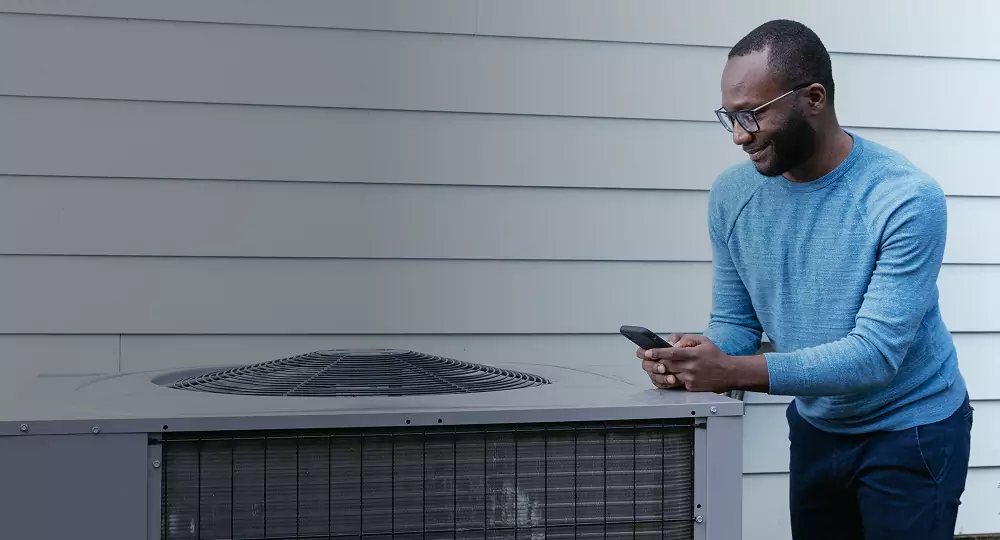 Man wearing a blue sweater inspecting a heat pump.