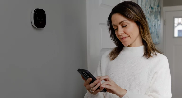 Woman checking her smart thermostat's settings from her cell phone.