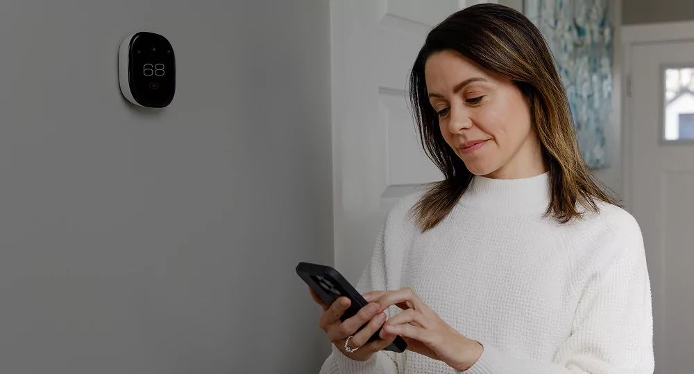 Woman checking her smart thermostat's settings from her cell phone.