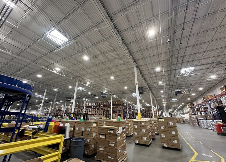 Wide interior view of a commercial distribution facility showcasing energy-efficient LED bay lights and skylights installed across high steel ceiling trusses.