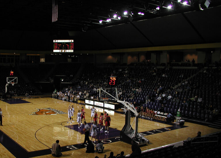 An indoor basketball game underway at Allen Arena, highlighting the high-intensity overhead stadium lighting system illuminating the court area and large-scale commercial facility infrastructure.