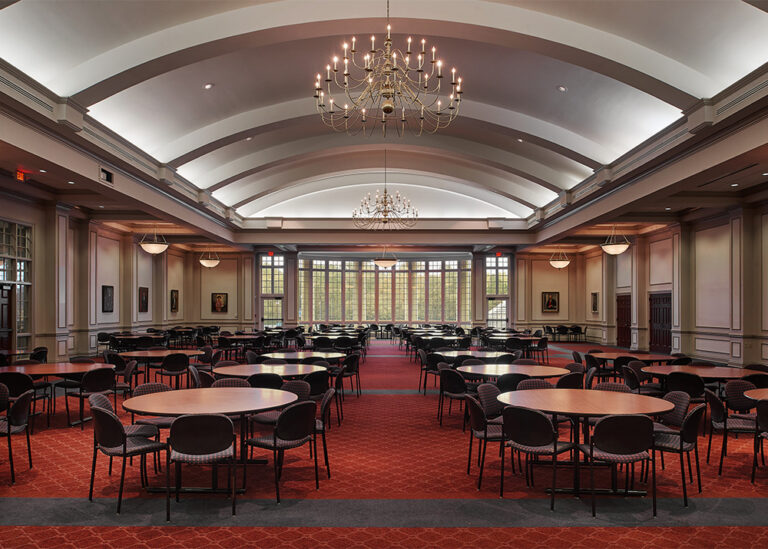 A large university dining facility at Memphis University School configured with rows of round tables, red carpeting, and an arched ceiling with elegant chandeliers.