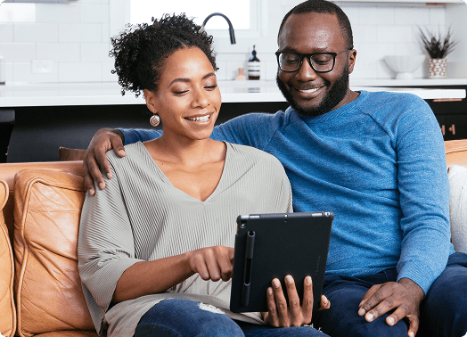A smiling couple on a couch looks at a tablet, exploring EnergyRight resources for their home's energy efficiency.