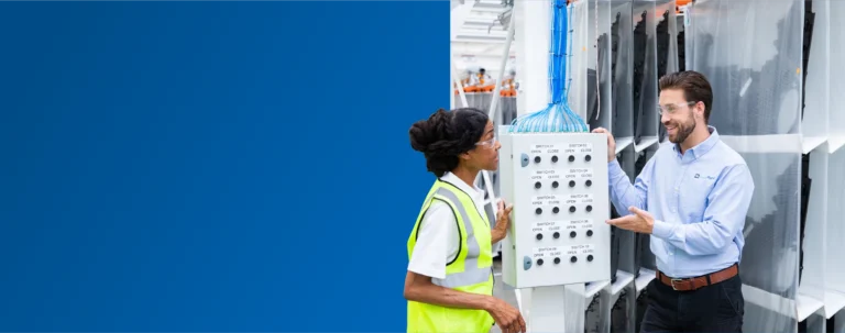 A TVA Energy Expert explains an industrial control panel with switches to another expert, demonstrating operational efficiency at a facility.
