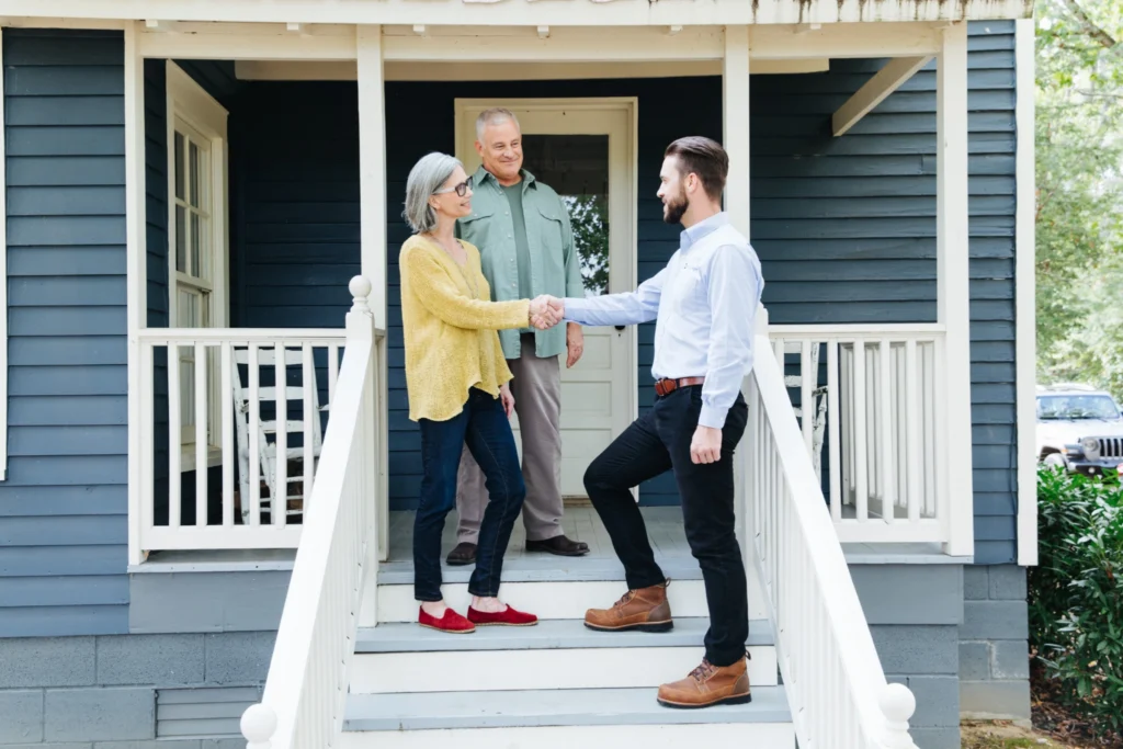 Middle-aged man and woman standing outside of their home, shaking hands with a TVA EnergyRight Energy Expert or a trusted, TVA-vetted member of the Quality Contractor Network.